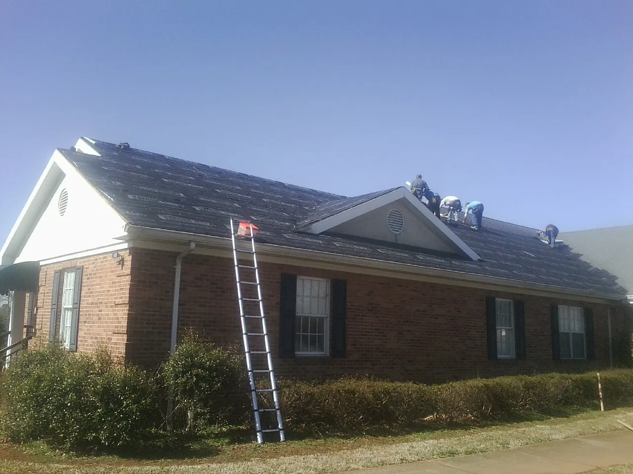 Crew tearing shingles off a brick ranch roof with a ladder set — Metal Roof Repair work by our crew in Jordan Valley