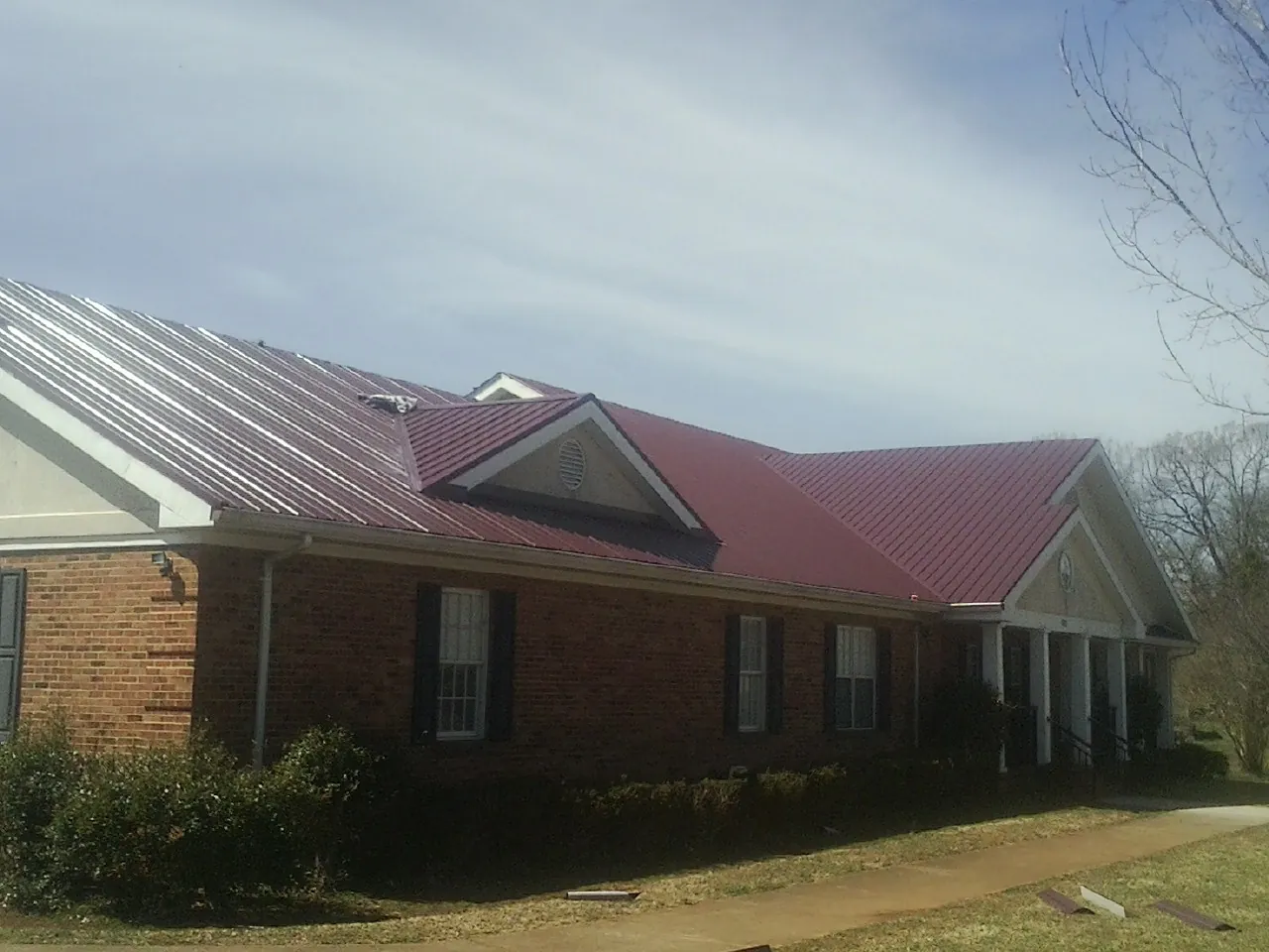 Red metal roof with gabled entries on a long brick building, from a Hail Damage Roof Repair job in Jordan Valley