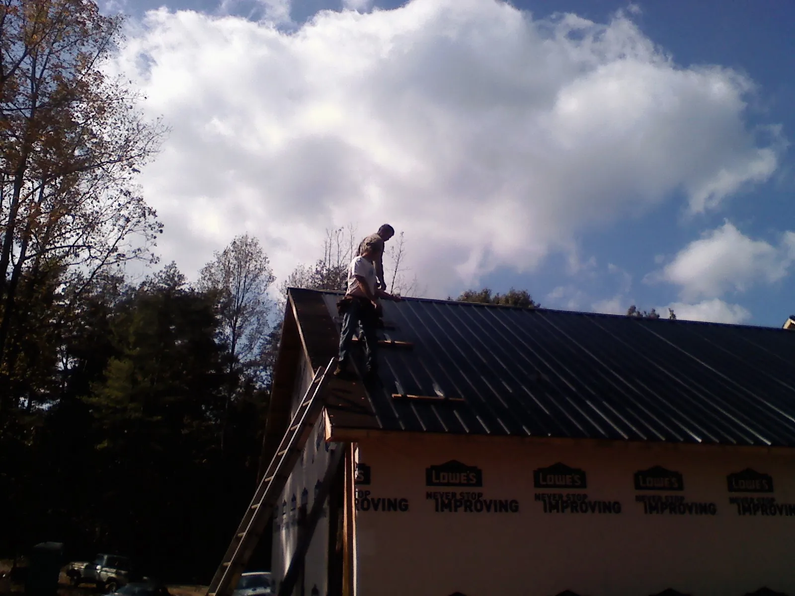 Roofer fastening dark metal panels high against a cloudy sky, from a Roof Inspection job in Jordan Valley