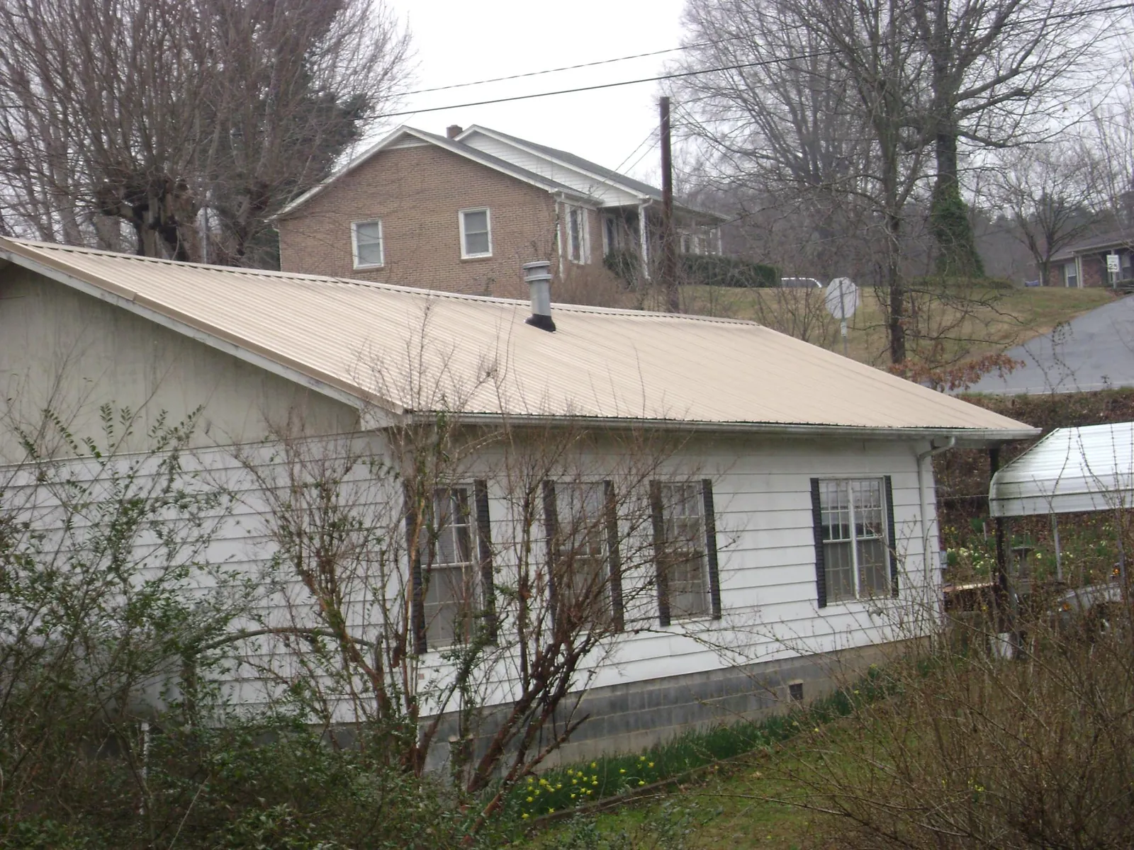 Tan metal roof on a white sided house set into a hillside — Commercial Roofing by Roofing Brothers in Jordan Valley