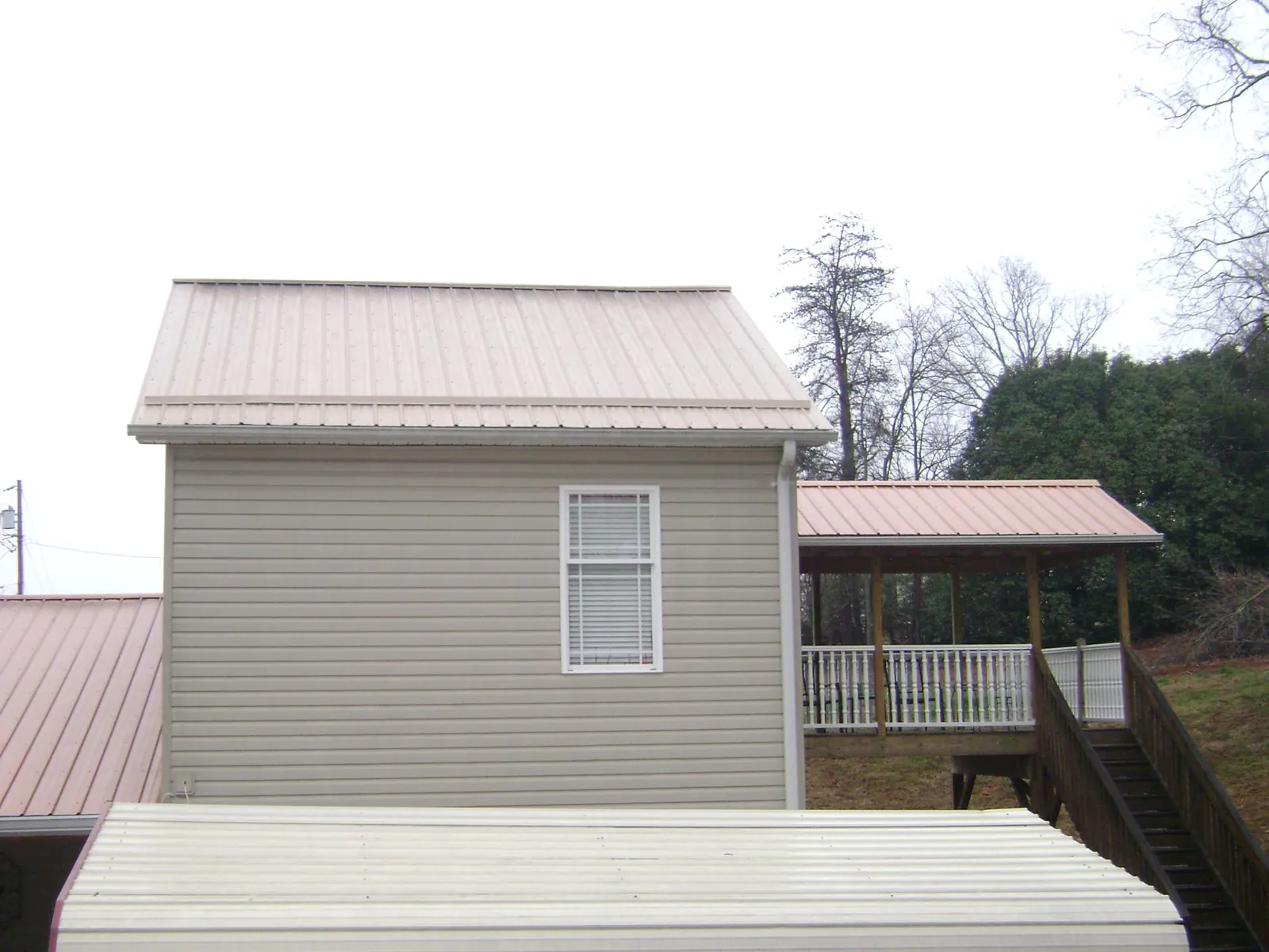Tan metal roofs on a two story addition and attached porch, from a Roof Replacement job in Jordan Valley